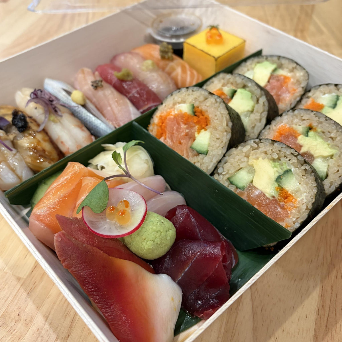 Omakase Set: nigiri, tamago with ikura, salmon avocado roll and assorted sashimi in a wooden box